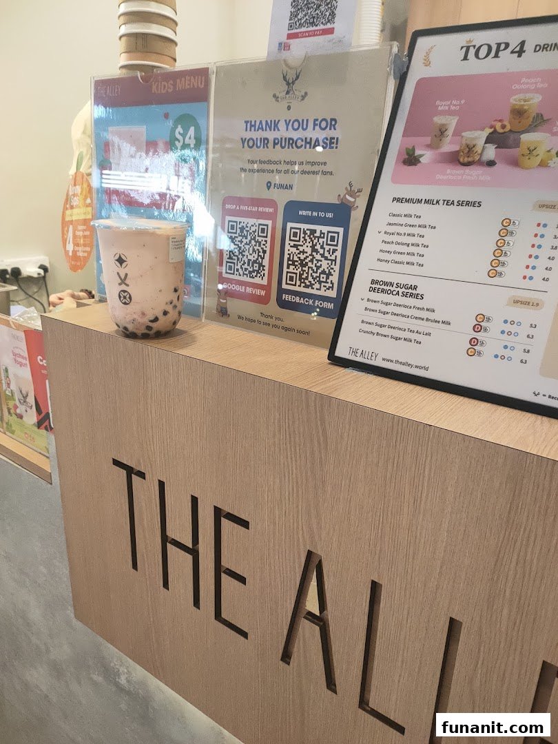 A counter at The Alley bubble tea shop, featuring a drink, menu board, and customer feedback signs.