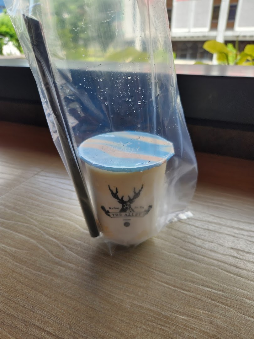 A refreshing bubble tea drink from The Alley, presented in a clear plastic bag with a straw.