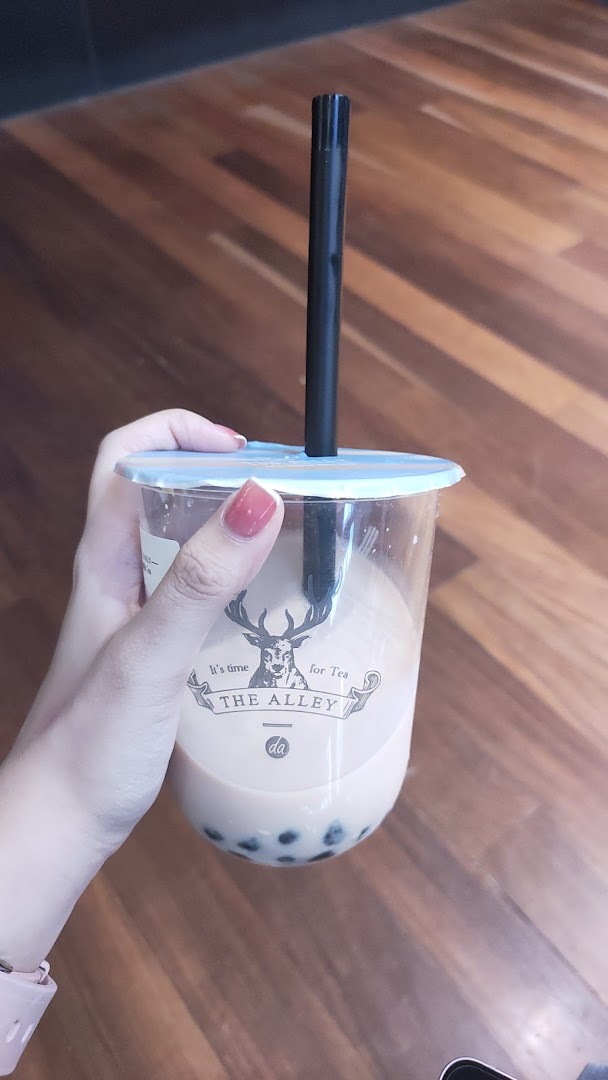 A hand holds a clear cup of bubble tea with tapioca pearls from The Alley.
