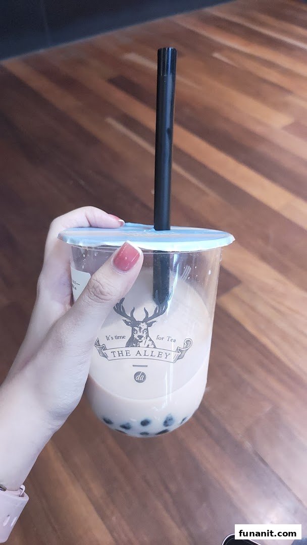 A hand holds a clear cup of bubble tea with tapioca pearls from The Alley.