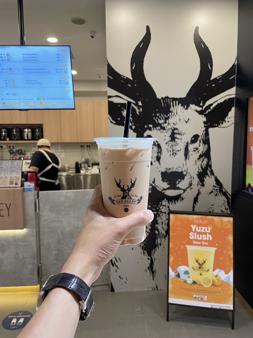 A hand holds a refreshing beverage inside The Alley, featuring a prominent deer mural and a menu screen.
