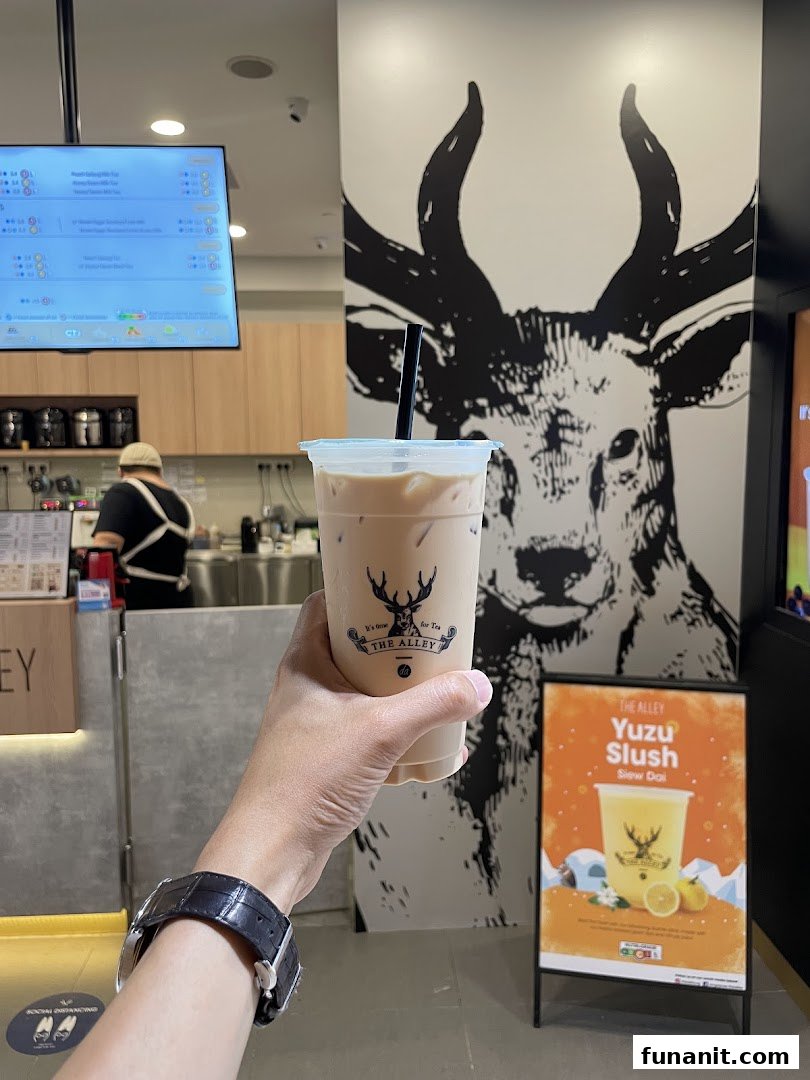 A hand holds a refreshing beverage inside The Alley, featuring a prominent deer mural and a menu screen.