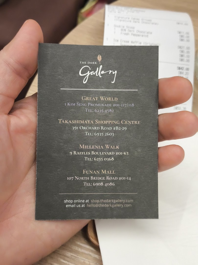 A hand holds a business card for The Dark Gallery, displaying multiple store locations and contact details.