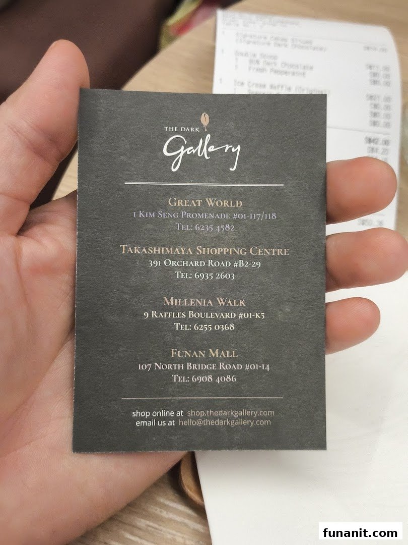 A hand holds a business card for The Dark Gallery, displaying multiple store locations and contact details.