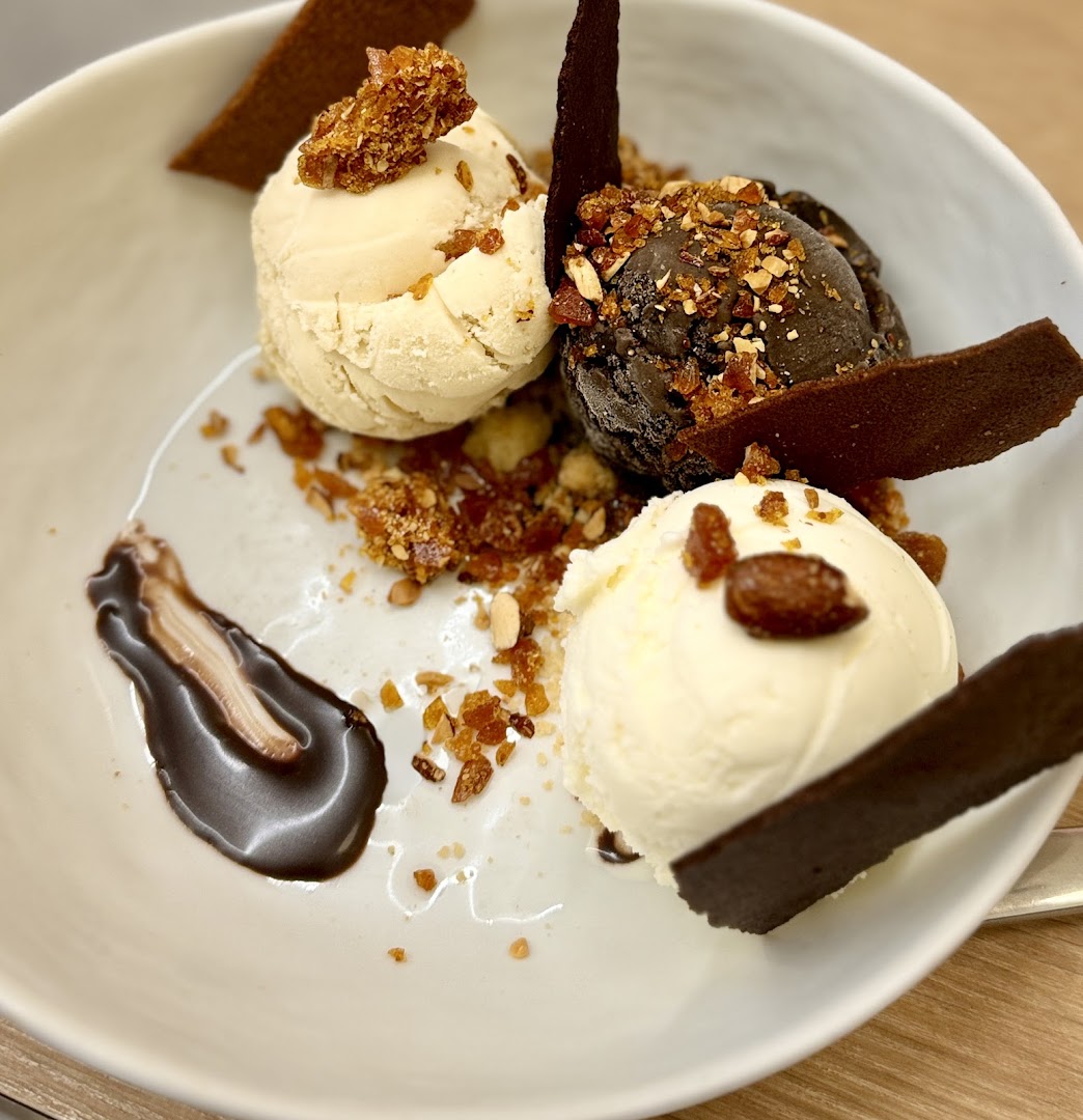 A bowl of gourmet ice cream with multiple scoops, chocolate, and crunchy toppings.