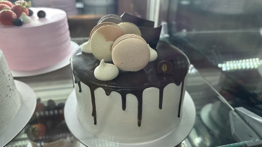 A display case showcasing beautifully decorated cakes, including a chocolate drip cake with macarons.