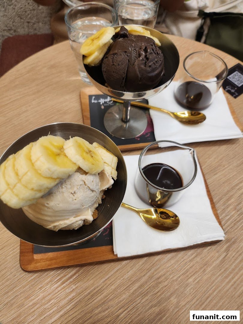 Two delicious ice cream sundaes with banana slices and chocolate sauce on a wooden table.