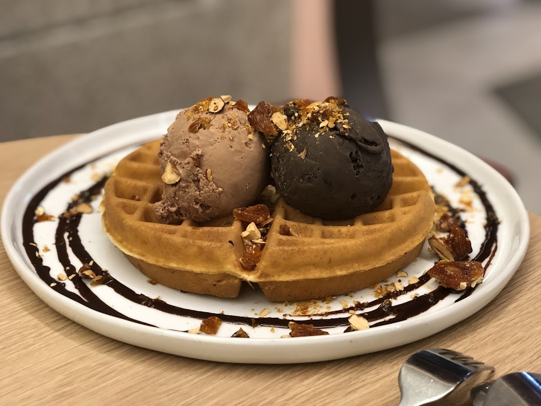A delicious waffle topped with two scoops of ice cream, chocolate drizzle, and nuts.