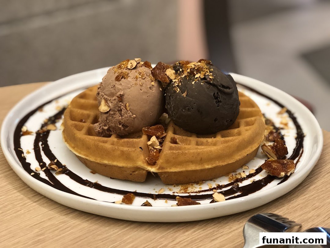 A delicious waffle topped with two scoops of ice cream, chocolate drizzle, and nuts.