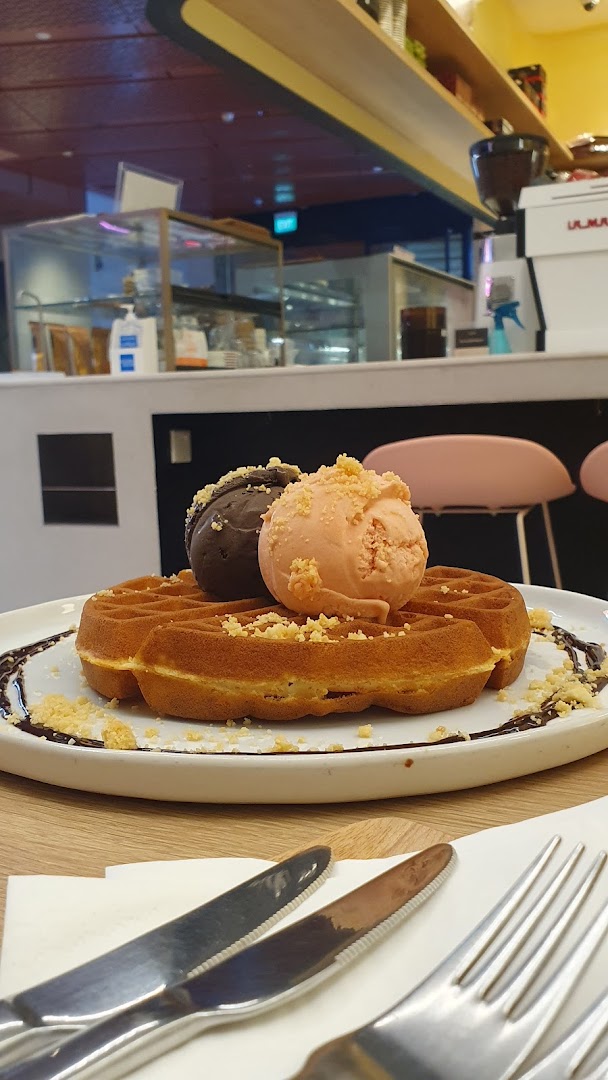 A delicious waffle topped with two scoops of ice cream and crumbs, served in a cafe setting.