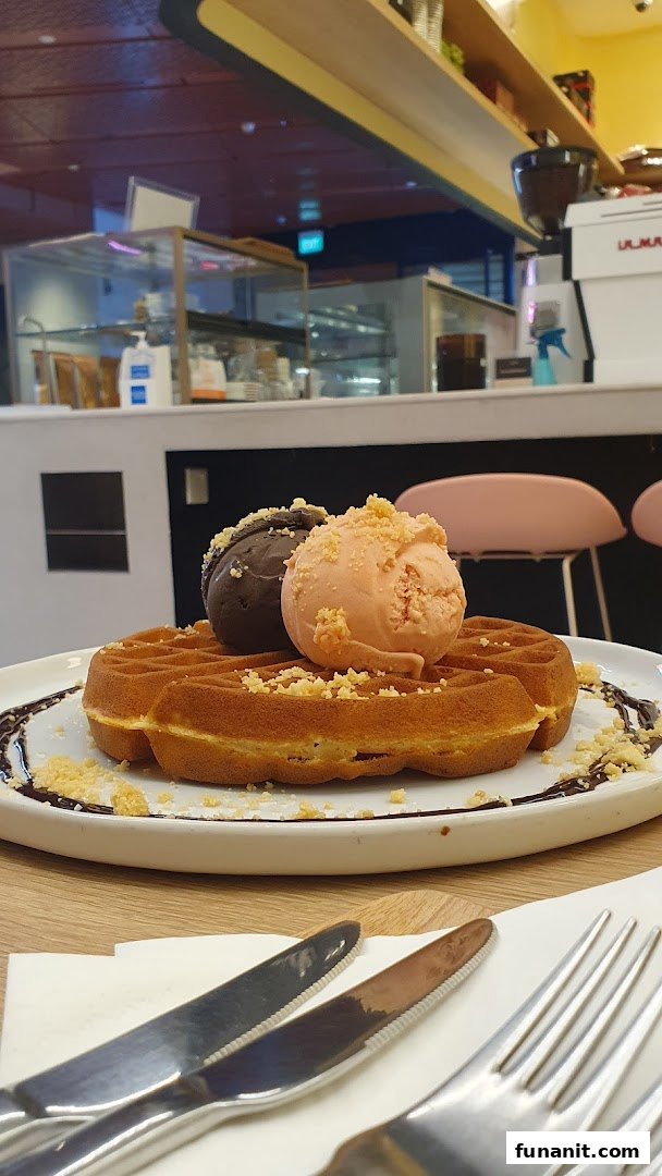 A delicious waffle topped with two scoops of ice cream and crumbs, served in a cafe setting.
