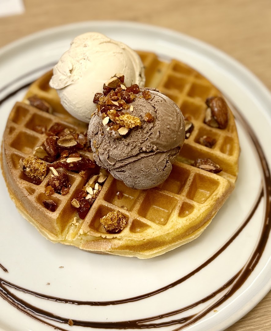 A delicious waffle topped with two scoops of ice cream, nuts, and chocolate drizzle.