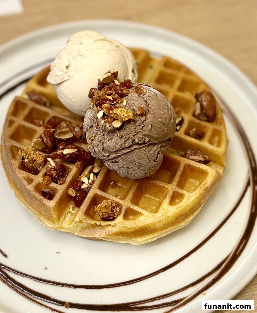A delicious waffle topped with two scoops of ice cream, nuts, and chocolate drizzle.