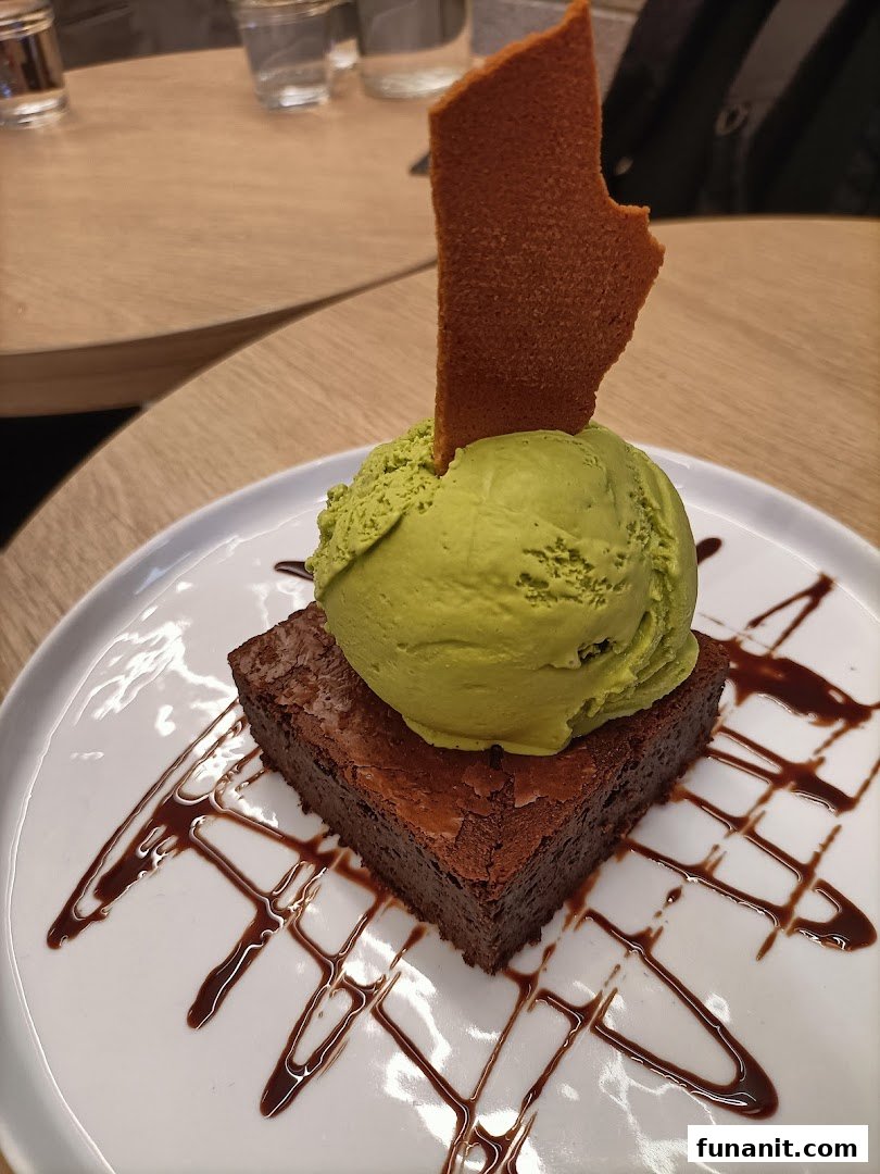 A rich chocolate brownie topped with a scoop of green ice cream and a crisp wafer.