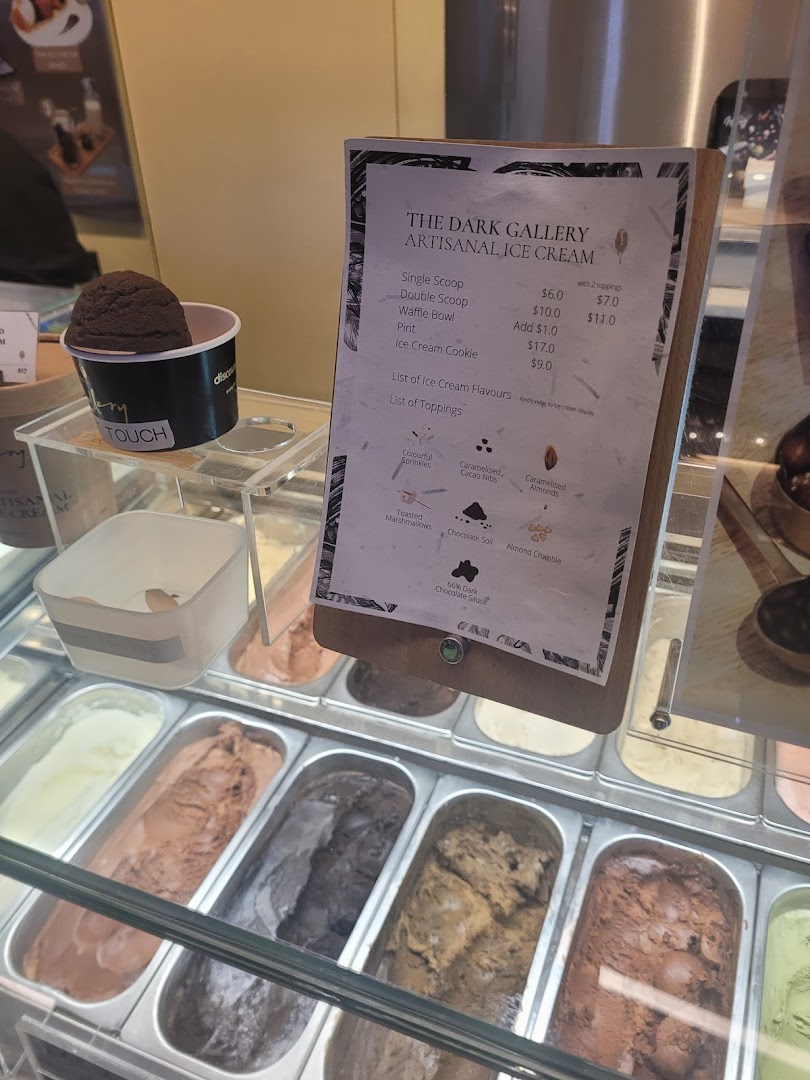 An ice cream display case showcasing various artisanal ice cream flavors, with a menu board detailing prices and toppings.