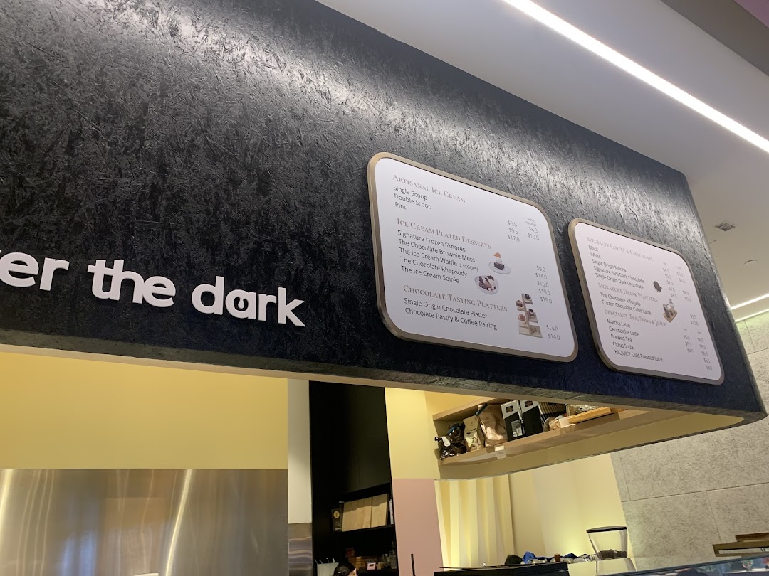 A close-up view of The Dark Gallery's menu boards displaying artisanal ice cream, plated desserts, and chocolate drinks.