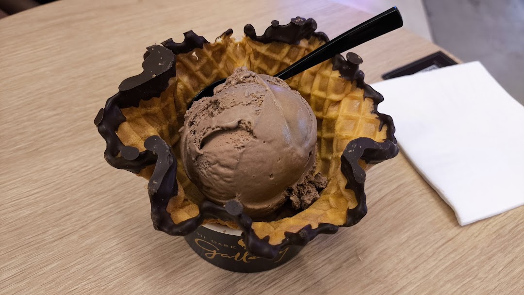 A scoop of chocolate ice cream served in a chocolate-dipped waffle bowl on a wooden table.