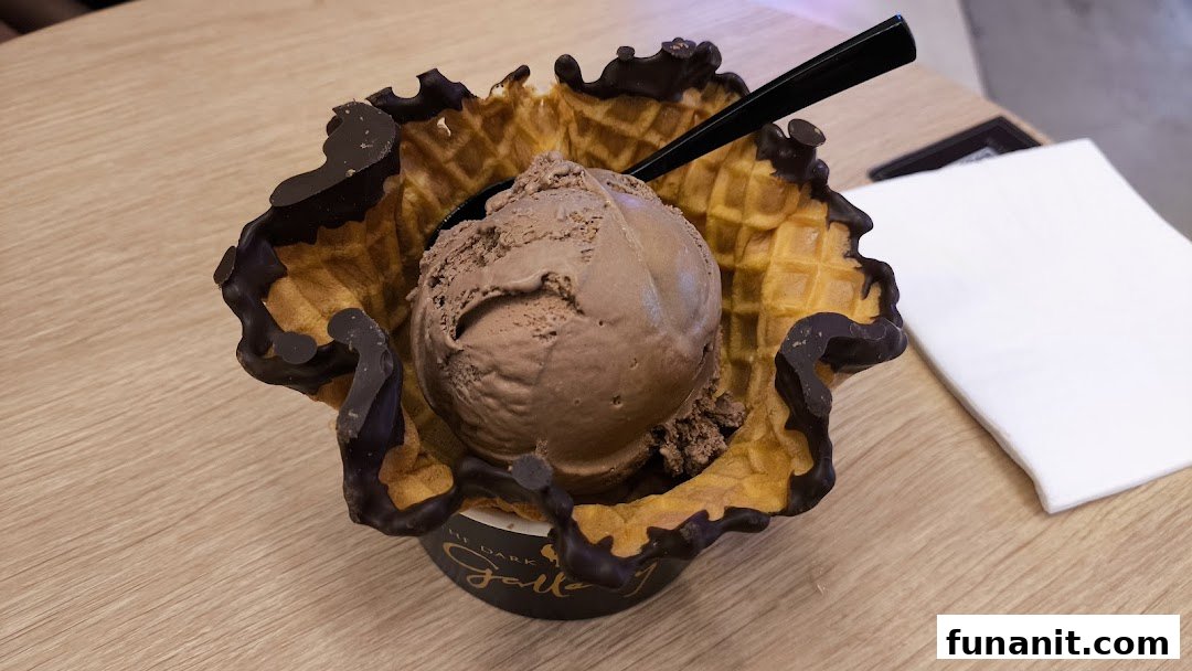 A scoop of chocolate ice cream served in a chocolate-dipped waffle bowl on a wooden table.