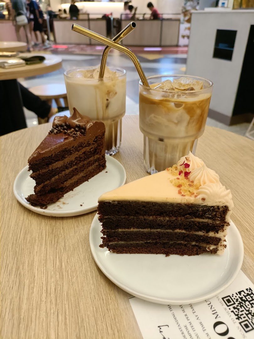 Two slices of layered cake and two iced beverages with metal straws on a wooden table.