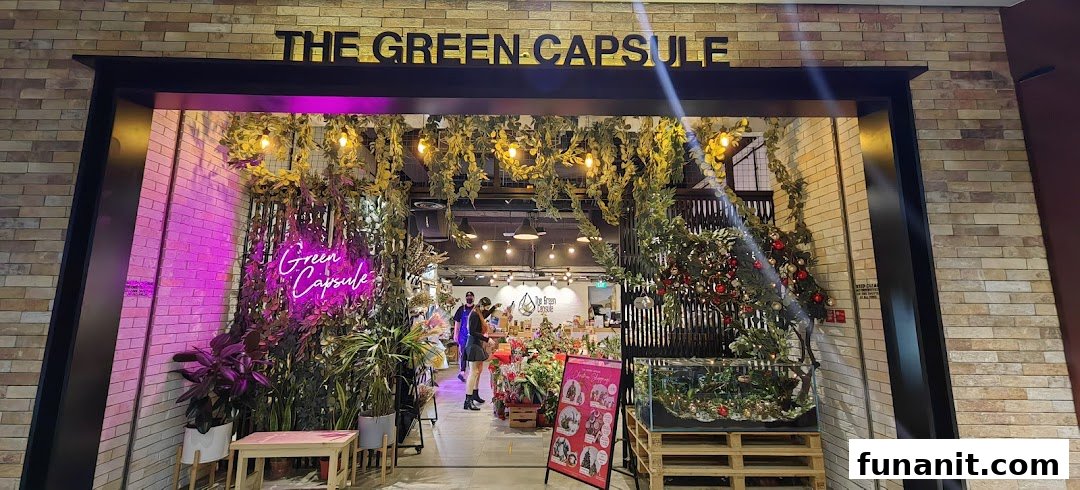 The entrance of 'The Green Capsule' shop, adorned with lush greenery, warm lights, and a vibrant neon sign.