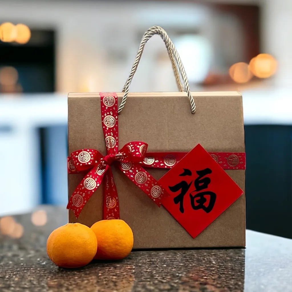 A festive gift box with red ribbon and Chinese character 'Fu' alongside two oranges.