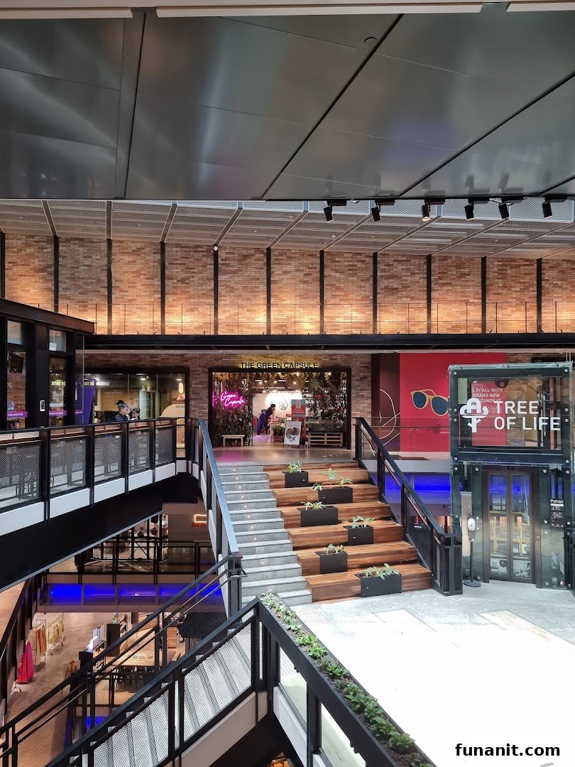 The Green Capsule shop entrance at the top of a grand staircase in a modern shopping mall.