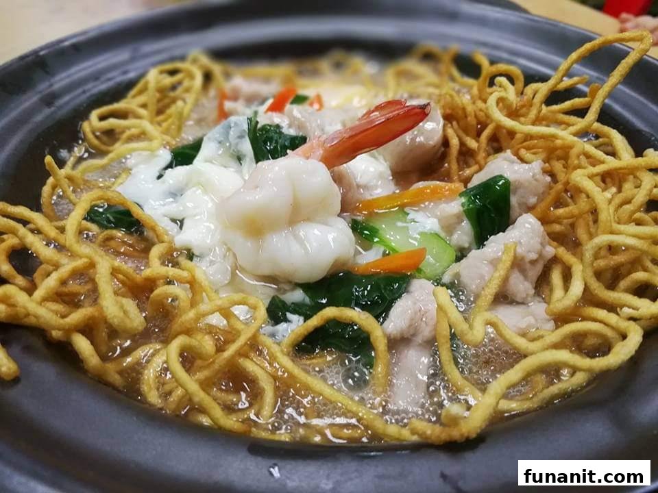 A close-up of a delicious claypot noodle dish with crispy noodles, shrimp, meat, and vegetables in savory gravy.