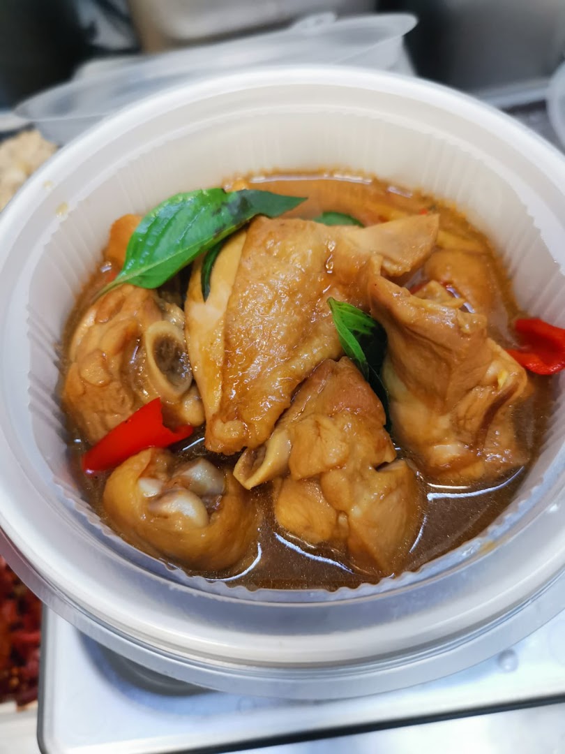 A close-up of a delicious chicken dish with basil and red chili in a plastic bowl.
