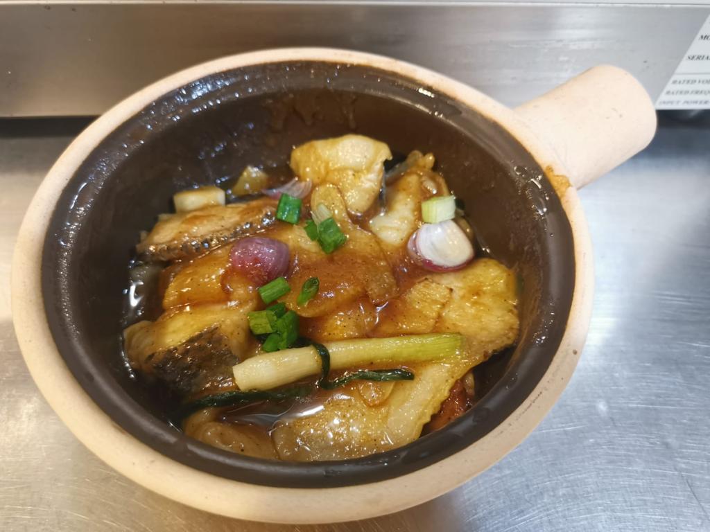 A delicious claypot dish featuring tender fish in a rich sauce, garnished with spring onions and red onions.