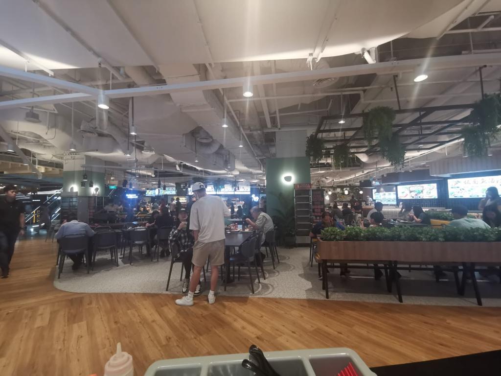 A wide view of a busy food court with diners, tables, and various food stalls.