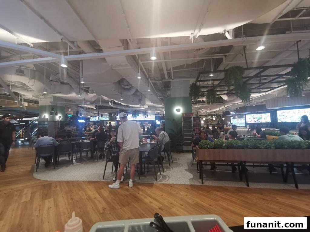 A wide view of a busy food court with diners, tables, and various food stalls.