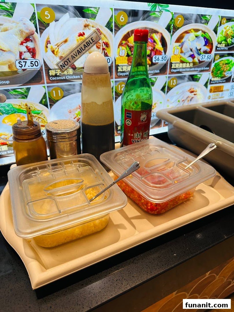 A digital menu board displaying claypot dishes and prices, with condiments on a counter.