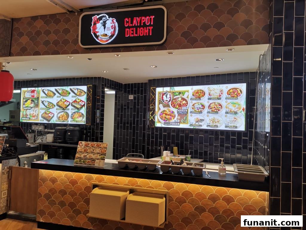 A food stall counter featuring digital menu screens displaying various claypot dishes and pricing.