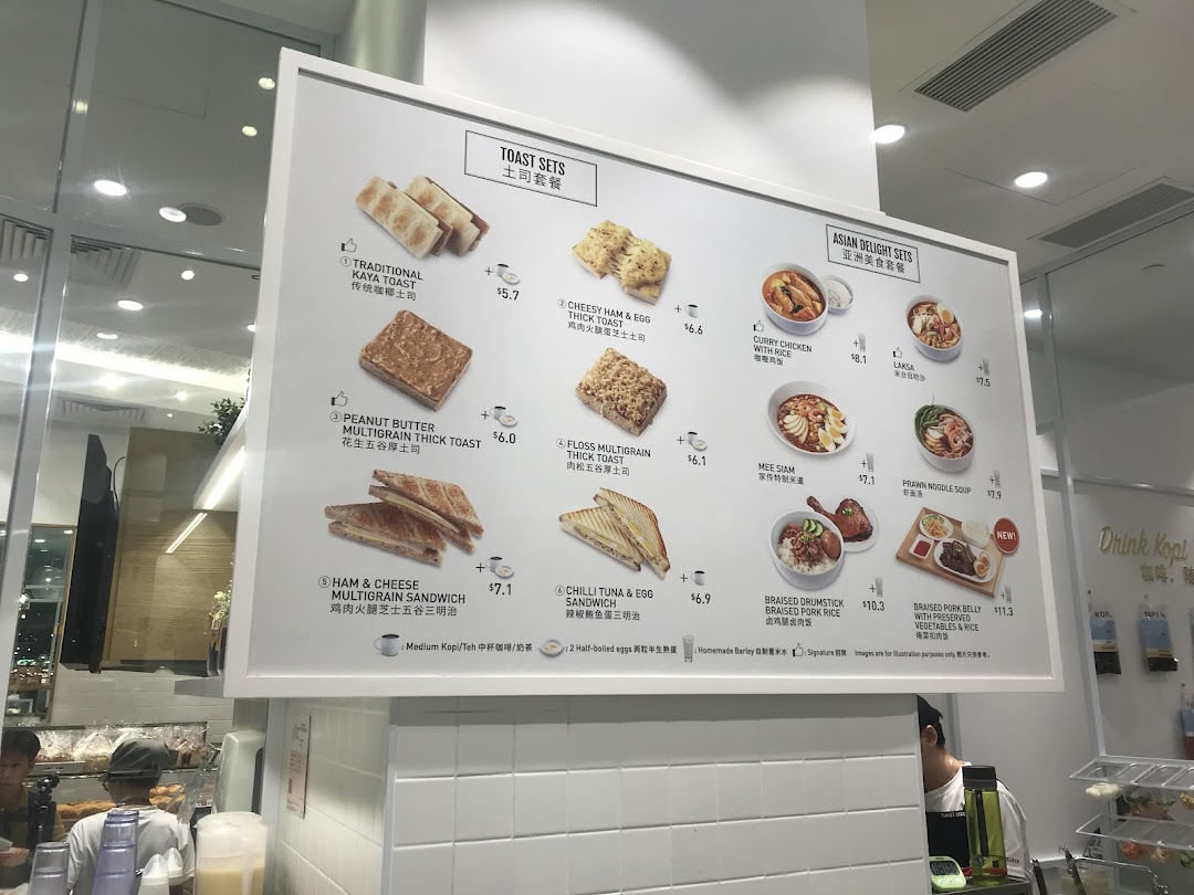 A brightly lit menu board at Toast Box Funan, showcasing a variety of toast sets and Asian delight meals.