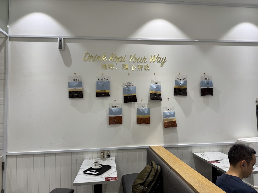 Interior view of Toast Box Funan, featuring a 'Drink Kopi Your Way' wall display and seating.