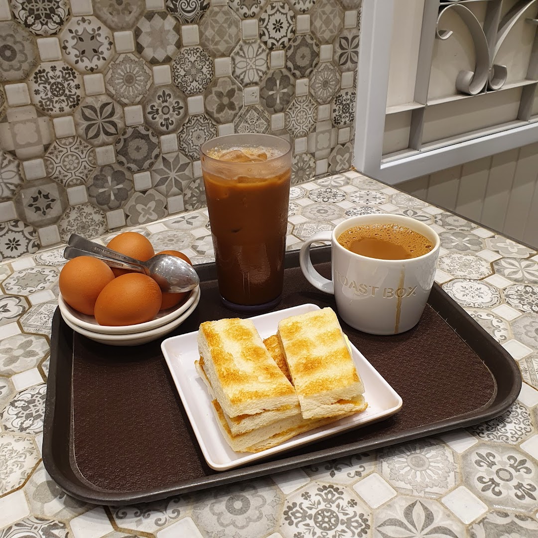 A classic Toast Box breakfast set with kaya toast, soft-boiled eggs, and coffee on a patterned table.