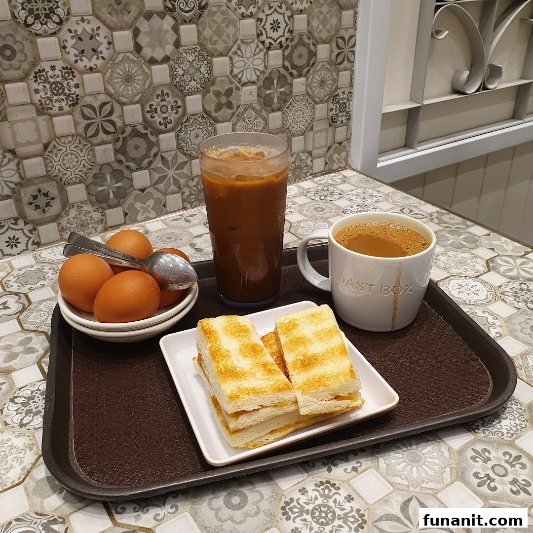 A classic Toast Box breakfast set with kaya toast, soft-boiled eggs, and coffee on a patterned table.