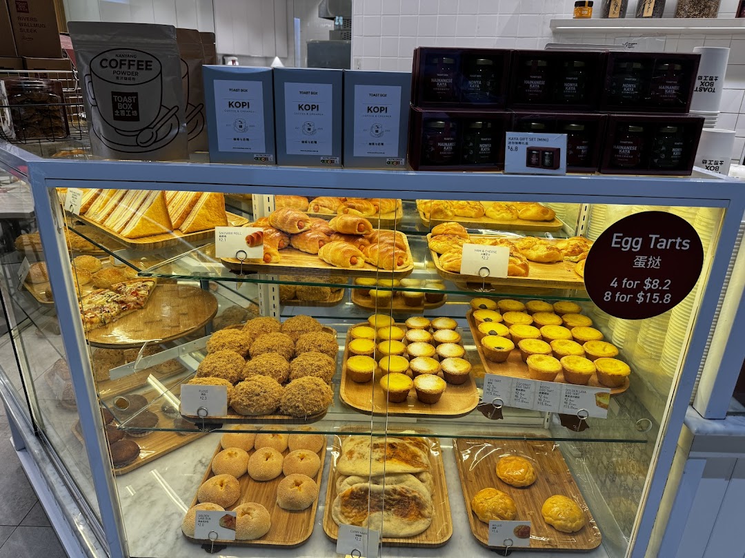 A display case at Toast Box showcasing a variety of freshly baked pastries, breads, and packaged coffee products.