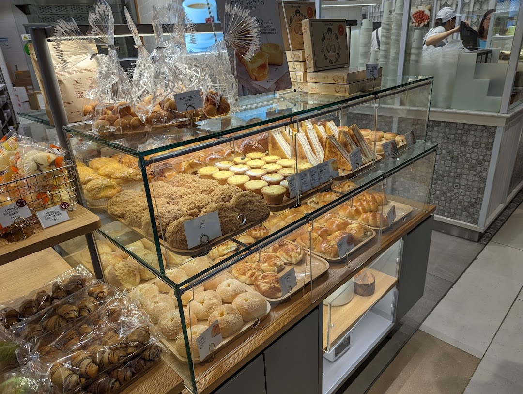 A glass display case showcasing a variety of freshly baked pastries, buns, and sandwiches at Toast Box.