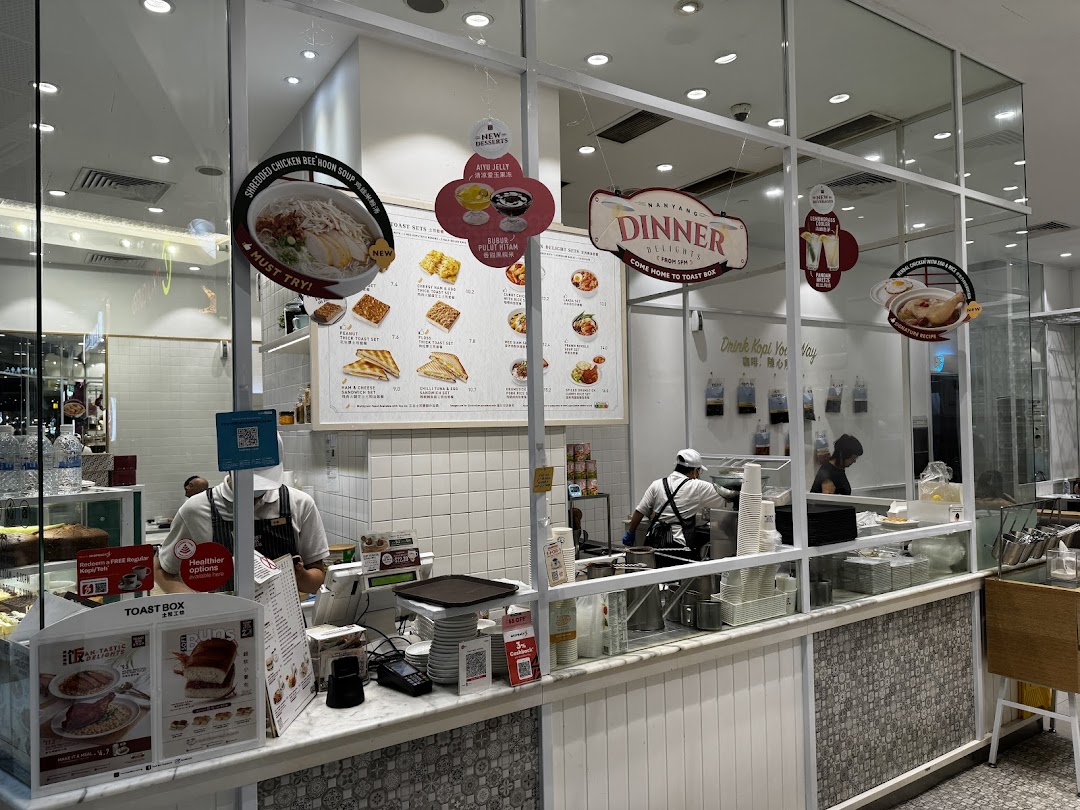 An interior view of Toast Box Funan, showcasing the counter, staff, and promotional menu displays.