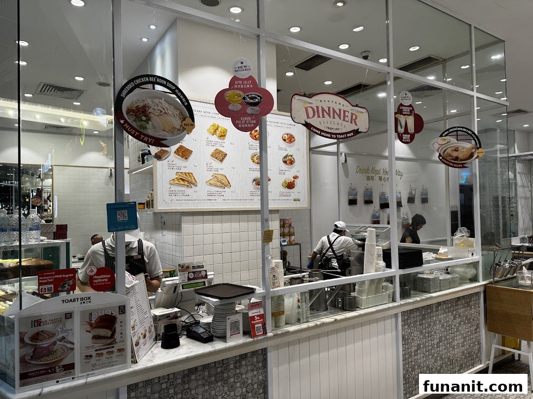 An interior view of Toast Box Funan, showcasing the counter, staff, and promotional menu displays.
