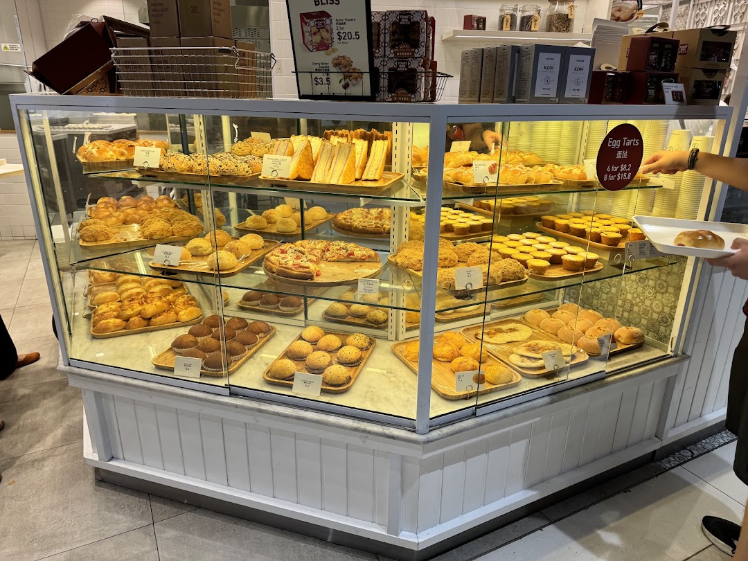 A vibrant display case showcasing a variety of freshly baked pastries, breads, and egg tarts at Toast Box.