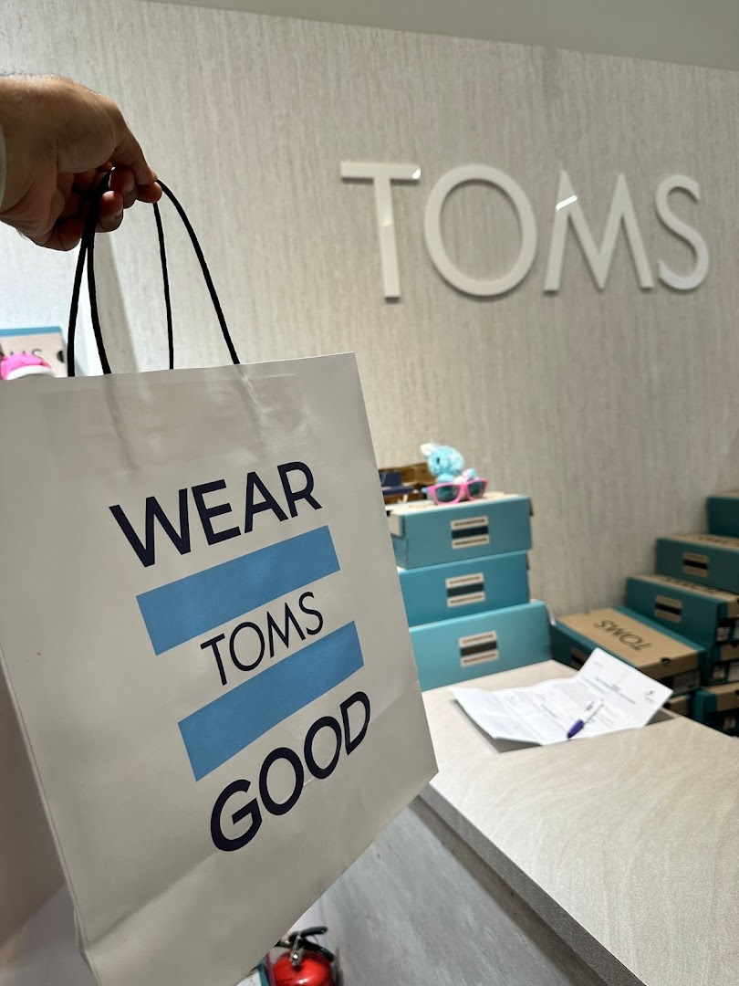 A customer holds a Toms shopping bag inside the store, featuring the brand's logo and merchandise.