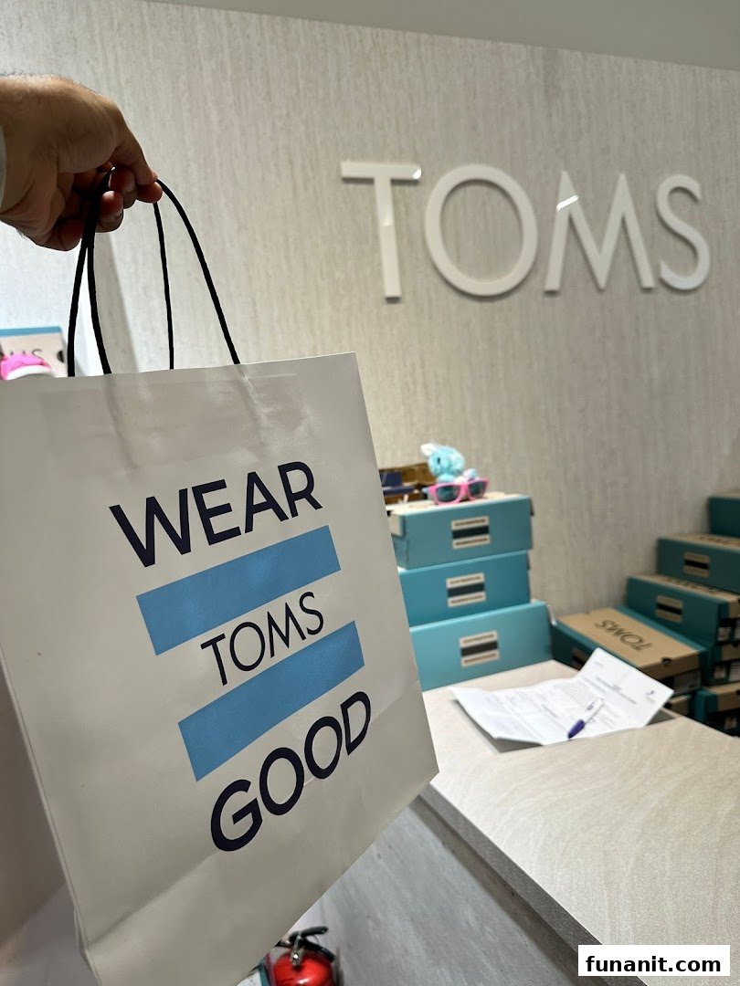 A customer holds a Toms shopping bag inside the store, featuring the brand's logo and merchandise.