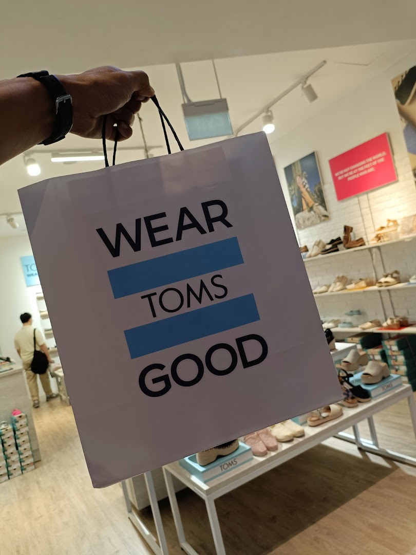 A person holds a TOMS shopping bag inside the store, showcasing the brand's message.