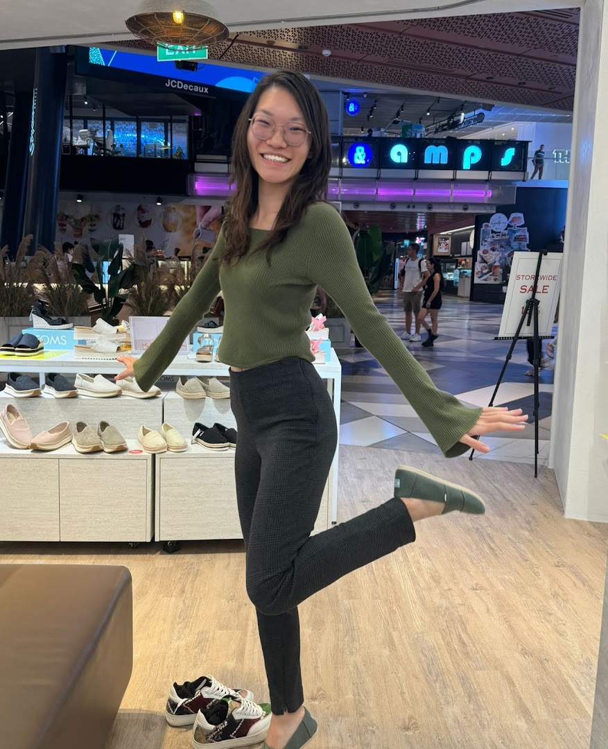 A woman playfully poses inside Toms shoe store, surrounded by various shoe displays.