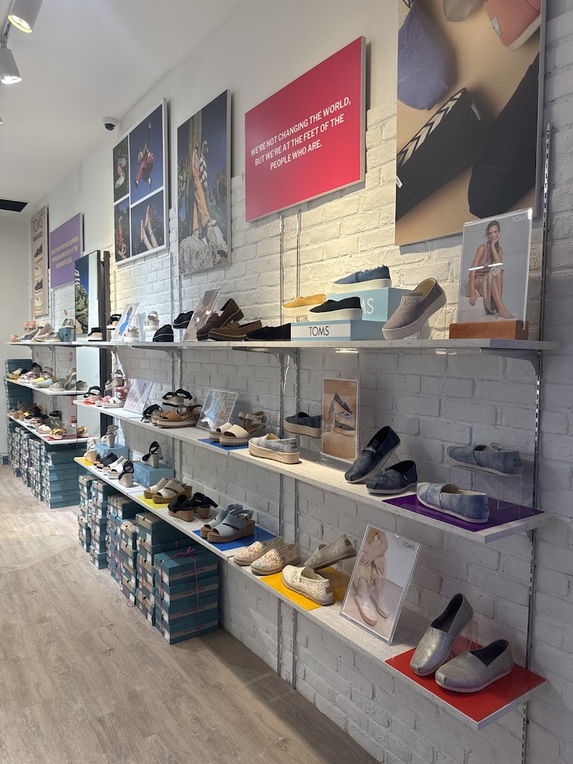 Interior view of Toms Funan showcasing various shoes on display shelves against a white brick wall.