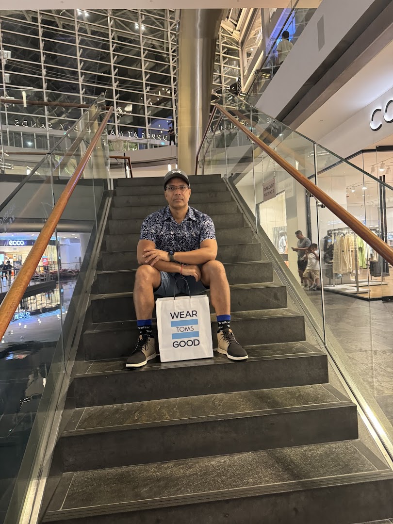 A man sits on mall stairs with a "Toms" shopping bag, showcasing his new purchase.
