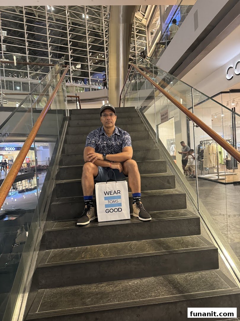 A man sits on mall stairs with a "Toms" shopping bag, showcasing his new purchase.
