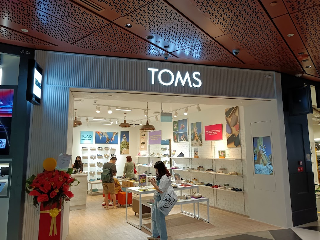 The bright and inviting storefront of TOMS at Funan, showcasing footwear and customers browsing.